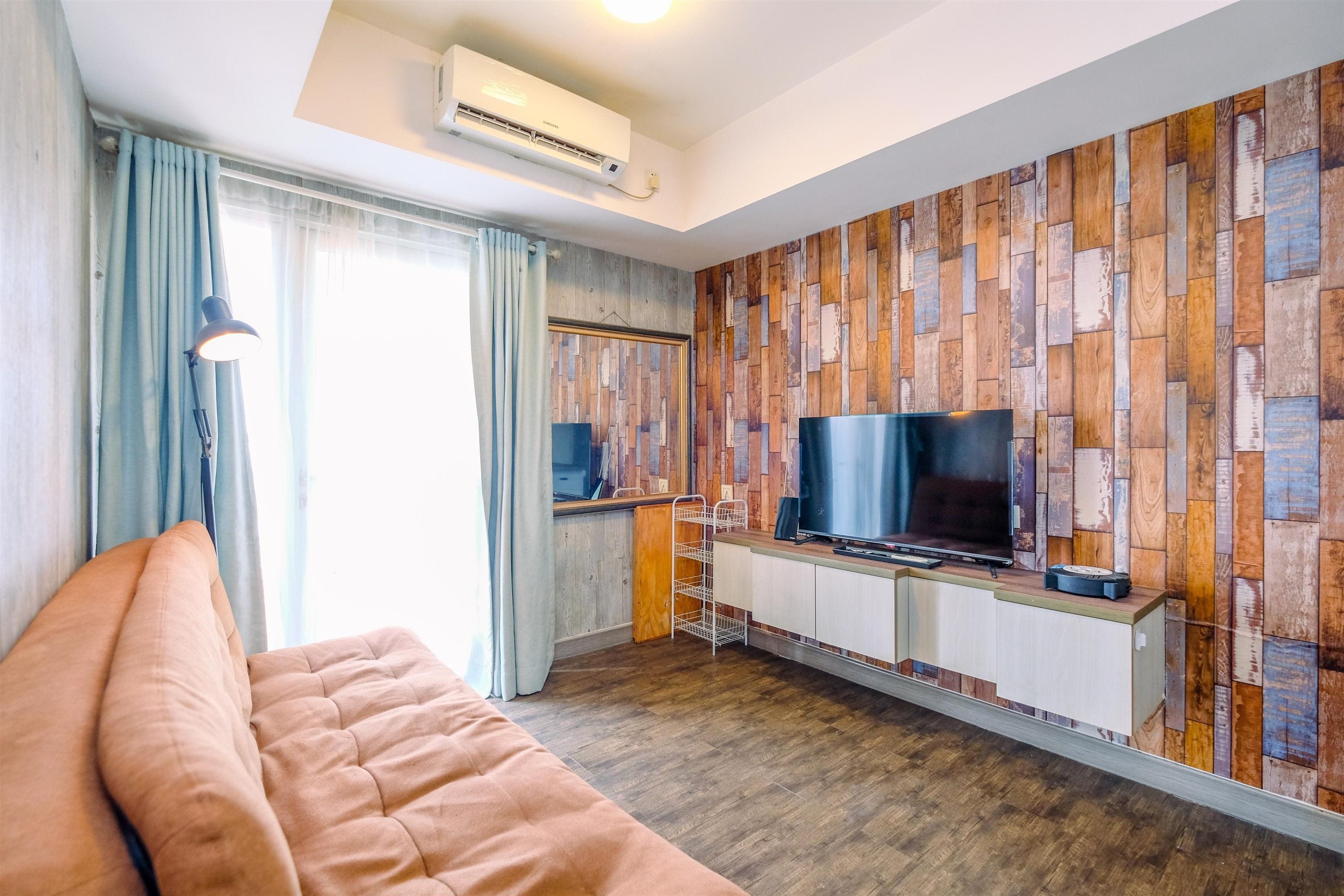 Habitación de hotel moderna con televisor de pantalla plana, un sofá, un escritorio con silla y una pared con diseño de tablones de madera.