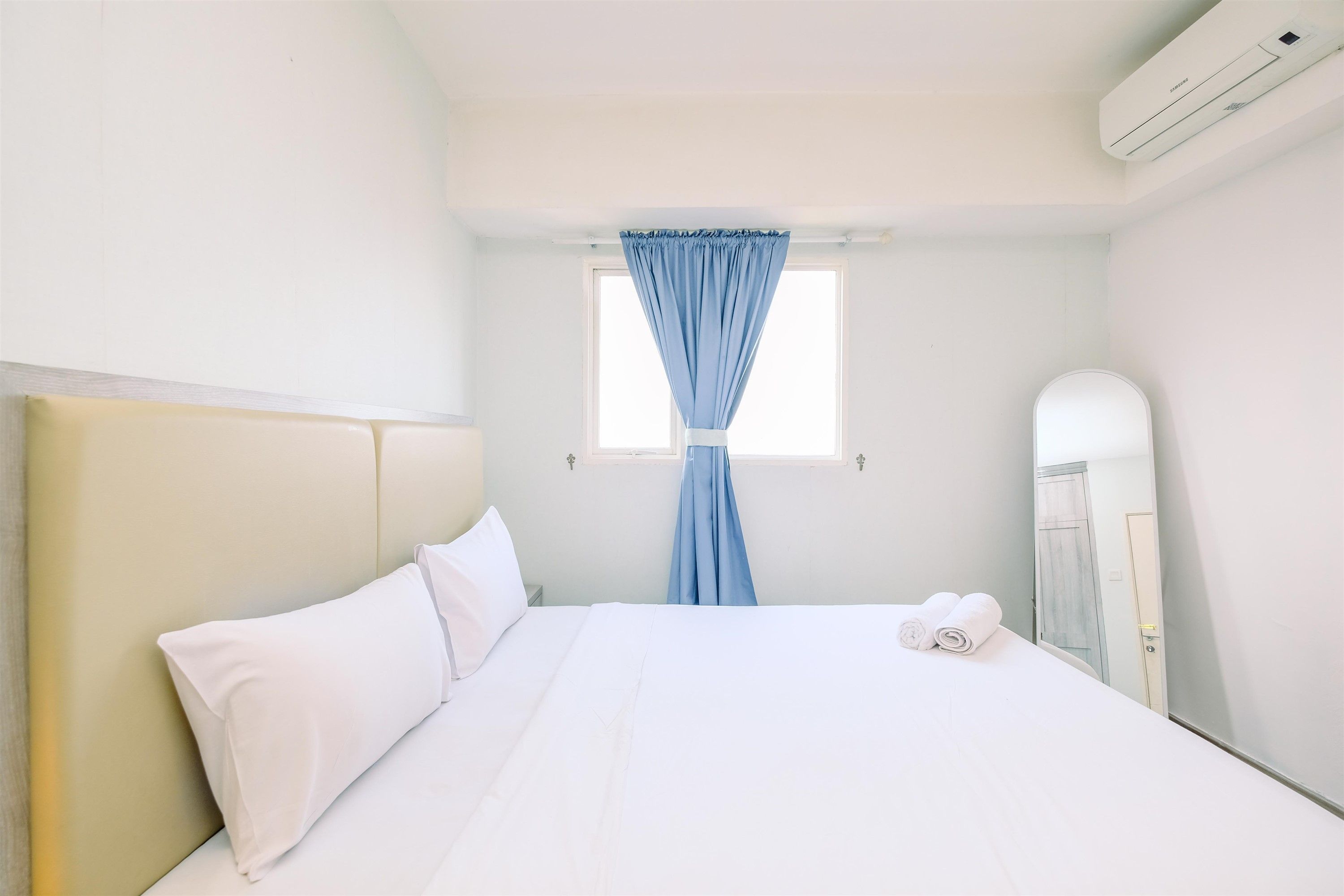 Habitación de hotel con cama, ventana con cortinas azules, unidad de aire acondicionado blanca y armario blanco.