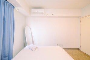 A hotel room with a bed, a wall-mounted air conditioner, a door, and a curtain. - Best Homey And Modern 1Br At The Wave Kuningan Apartment (Jakarta)