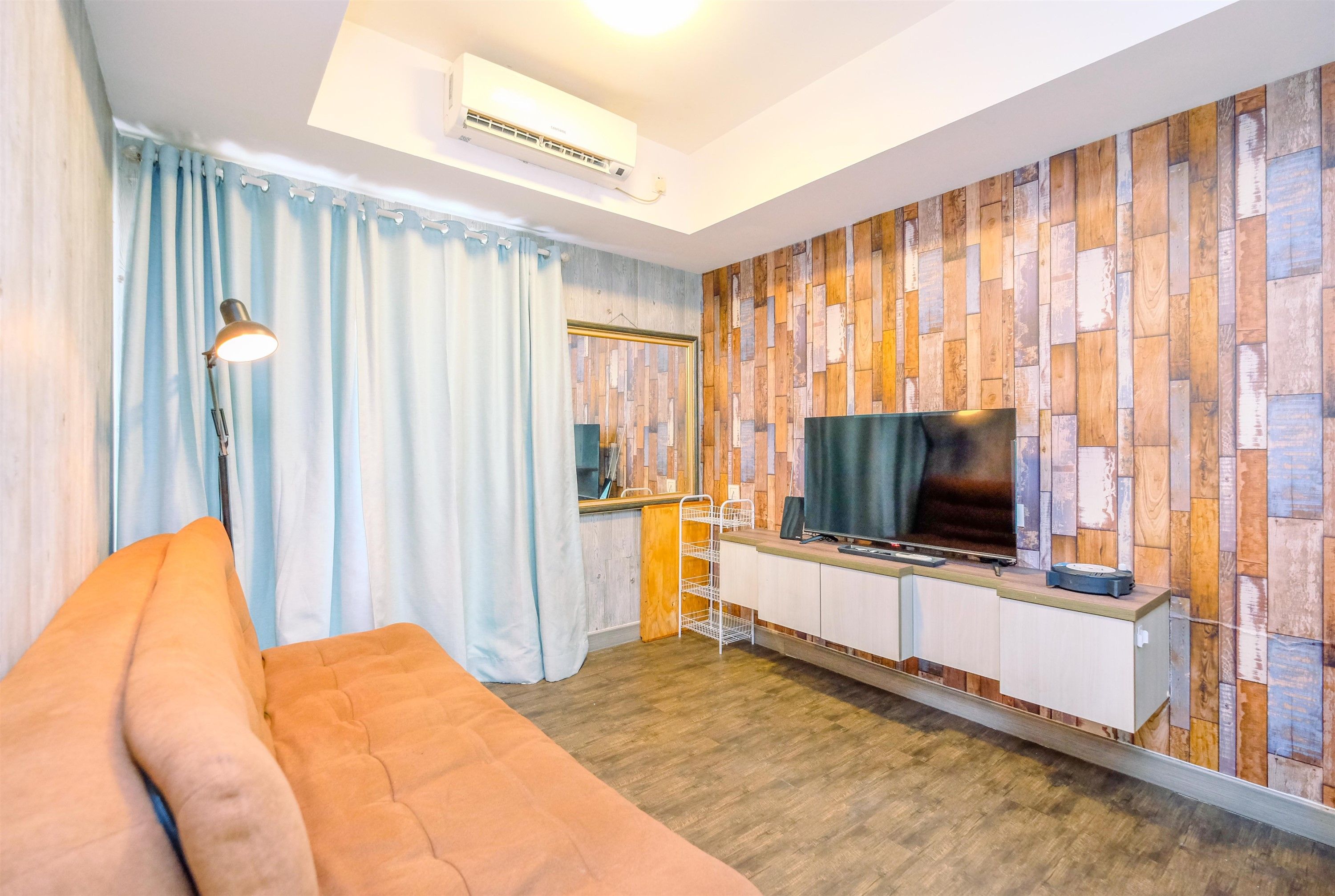 A modern living room with a sofa, a TV, a kitchenette, and a wooden wall panel.