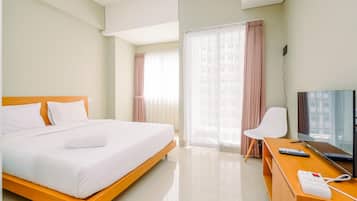A hotel room with a bed, a desk with a TV, and a window with curtains.