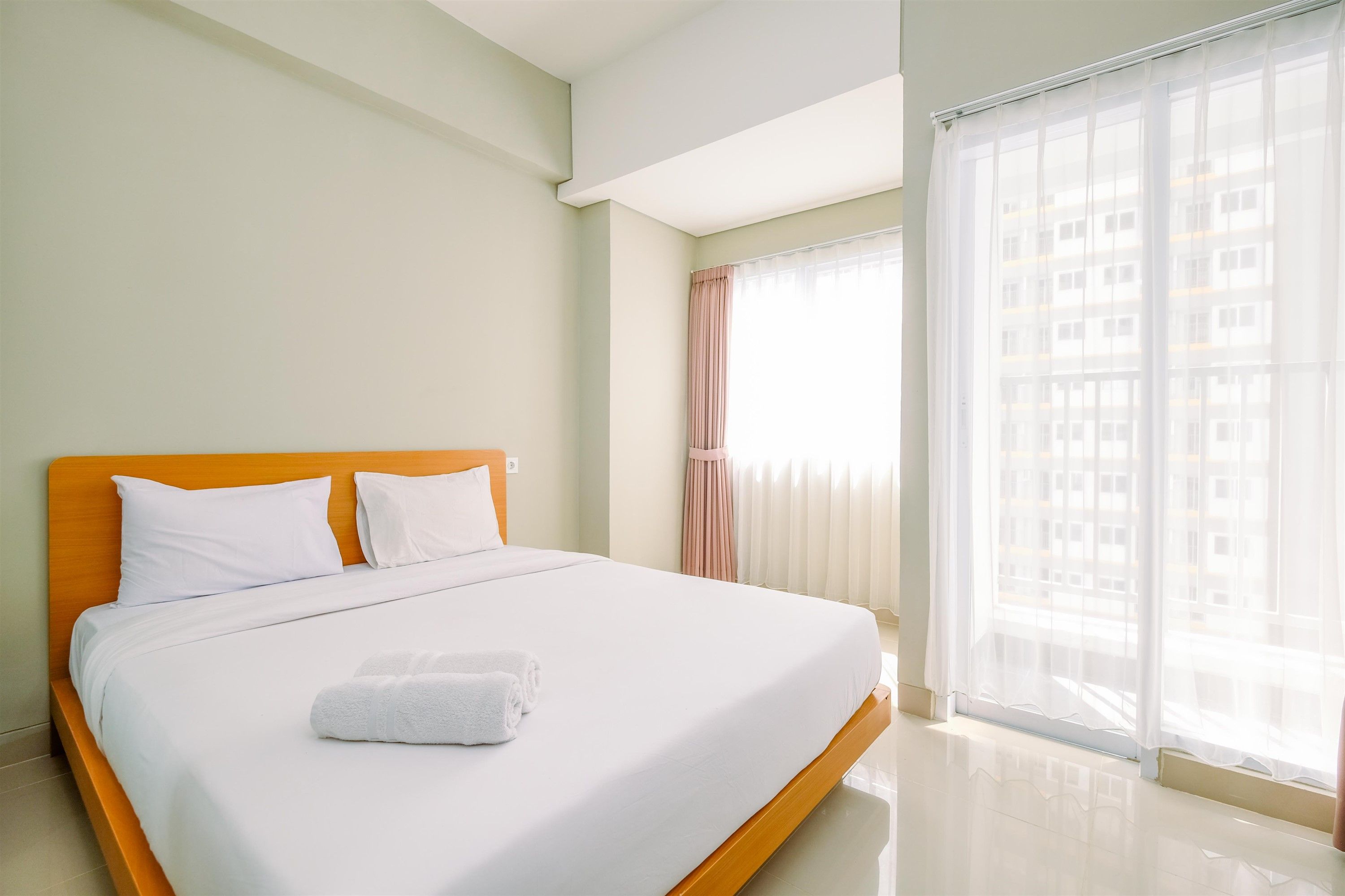 A hotel room with a bed, a window with curtains, and a view of buildings outside.