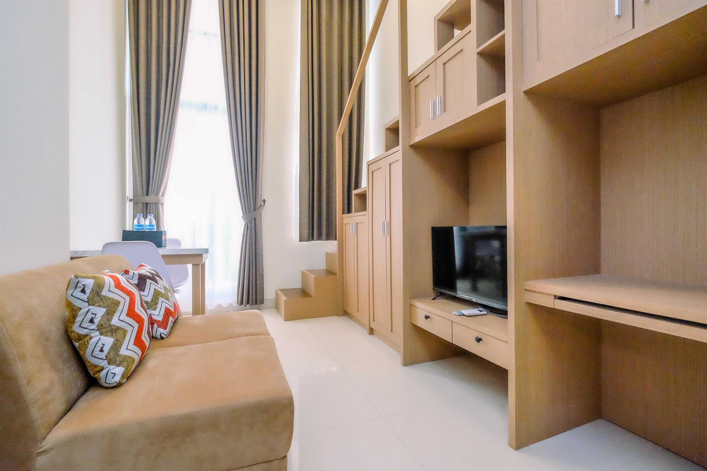 A modern living room with a sofa, a flat-screen TV, built-in wooden shelving, and a staircase.