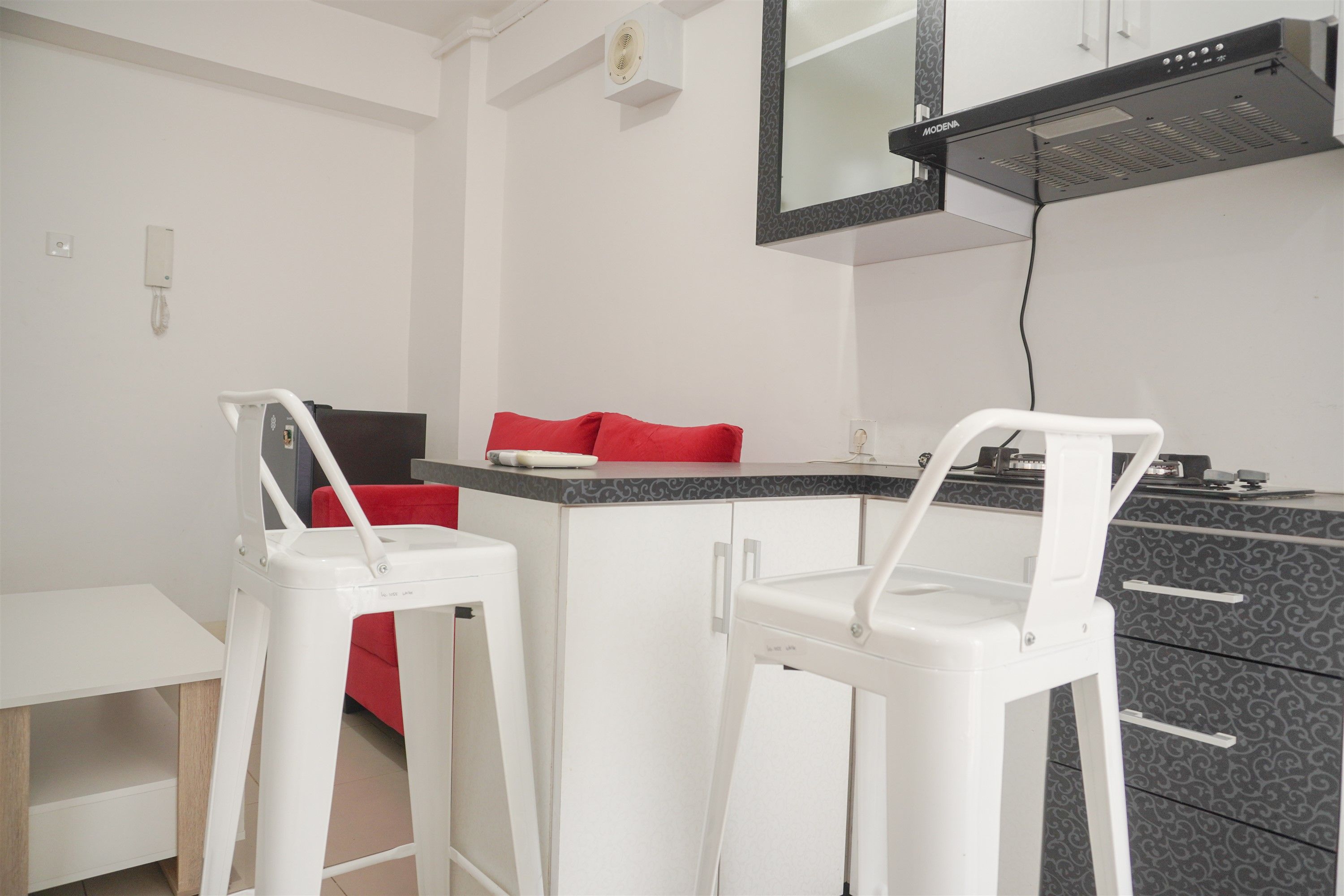 A small kitchenette with a microwave, a coffee maker, and a toaster. There are two white bar stools with red cushions.