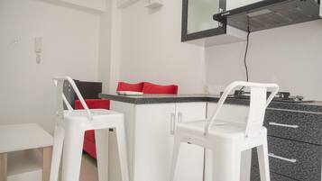 Een kleine kitchenette met een magnetron, een koffiezetapparaat en een broodrooster. Er staan twee witte barstoelen met rode kussens.