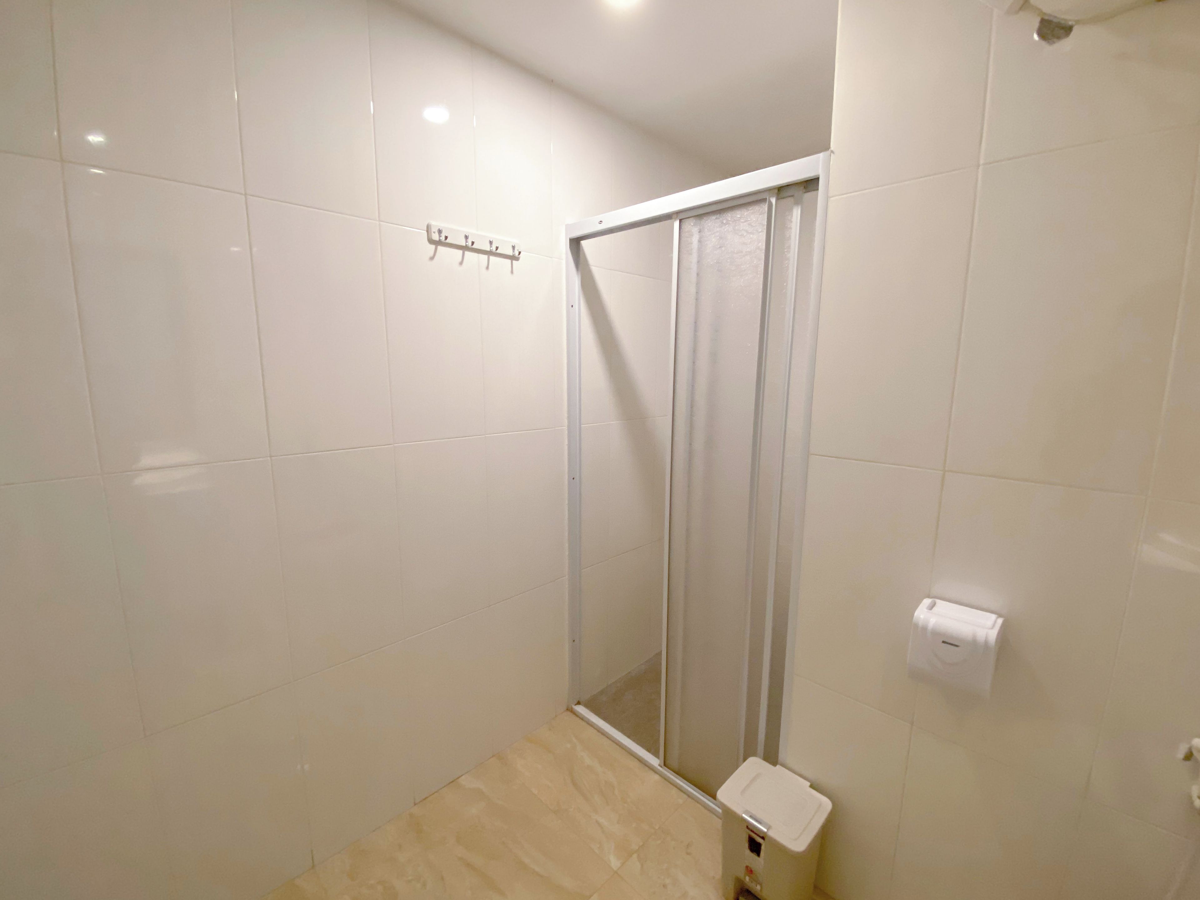 Un baño con azulejos blancos, una ducha con puerta de cristal y un dispensador de papel higiénico.