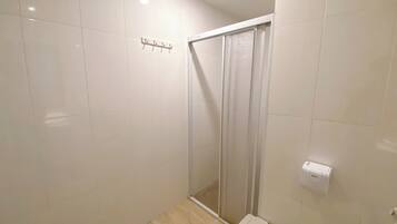 Un baño con azulejos blancos, una ducha con puerta de cristal y un dispensador de papel higiénico.