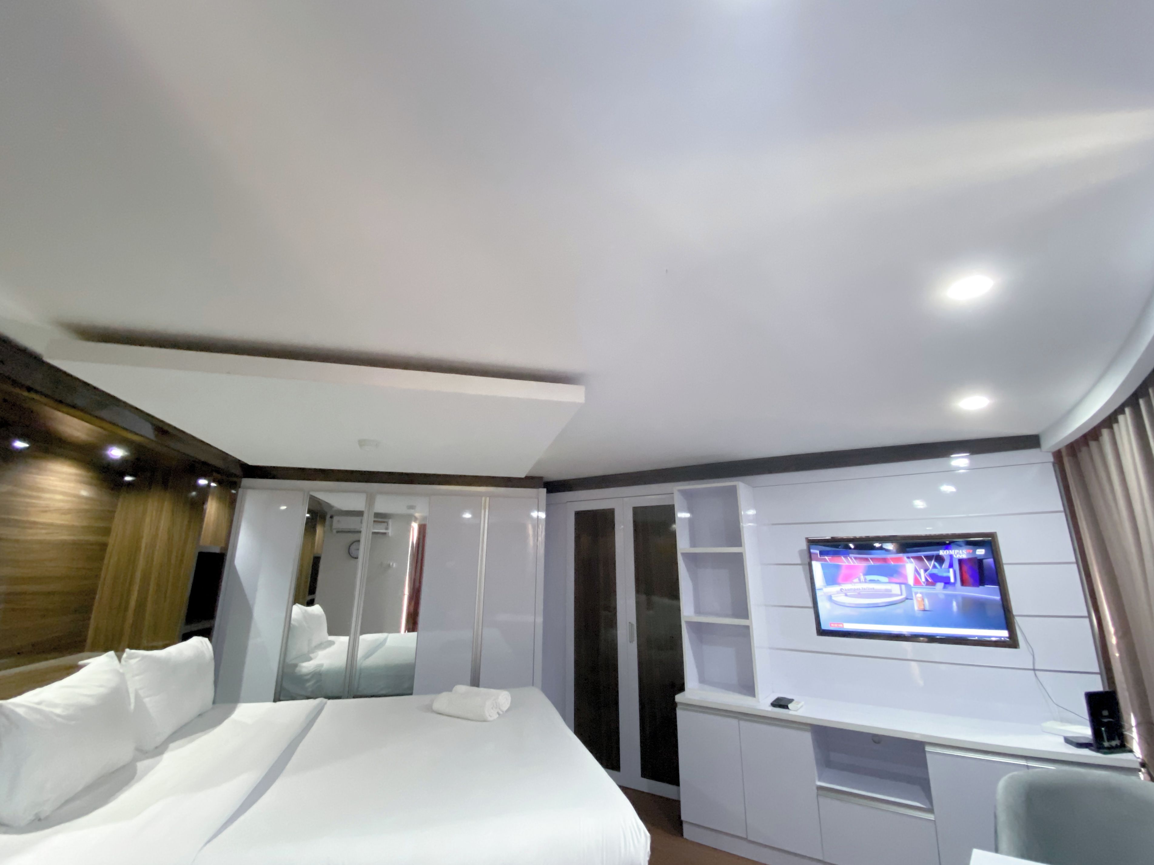 Una habitación de hotel con una cama grande, un televisor montado en la pared y un escritorio con una silla.