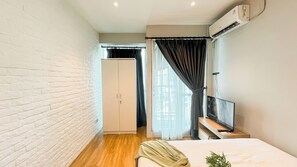 Habitación de hotel con pared de ladrillo, piso de madera, cama con manta verde, televisor y aire acondicionado.