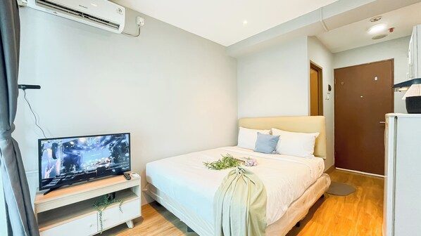 Una habitación de hotel con una cama, un televisor sobre un soporte de madera, un aire acondicionado instalado en la pared y una puerta.