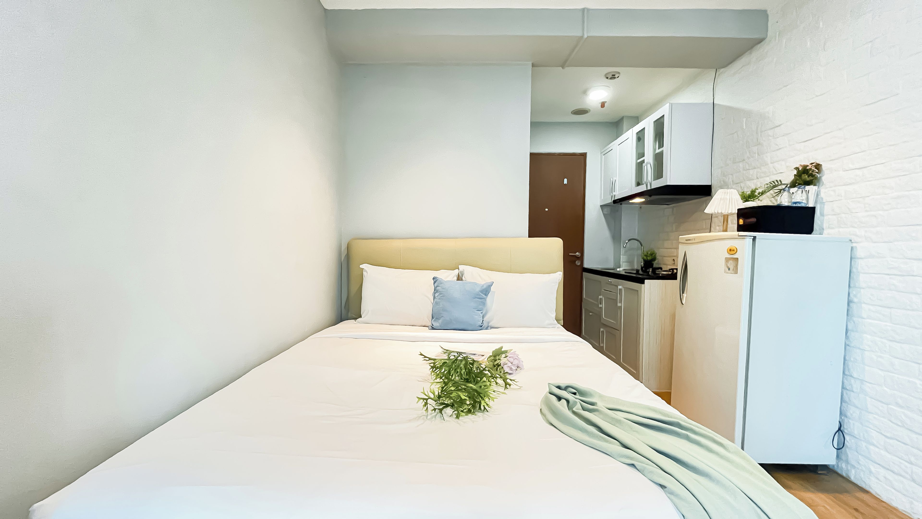 Une petite chambre propre, avec un lit, une table de chevet, une lampe et un réfrigérateur.