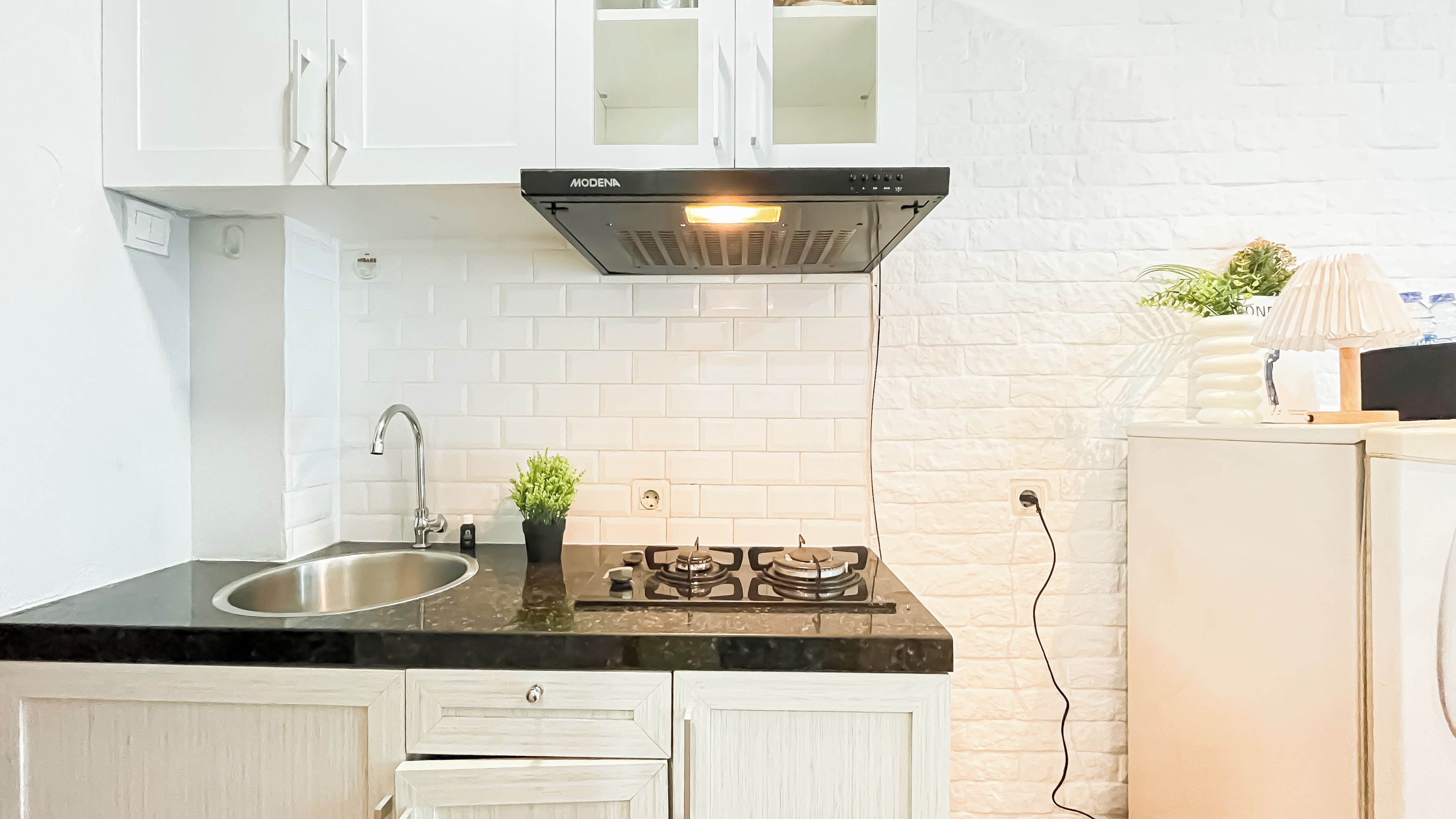 A kitchen with white cabinets, a stainless steel sink, a gas stove, and a white brick backsplash.