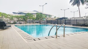 Ein Pool im Freien mit Metallgeländer, umgeben von einer gefliesten Liegefläche und einem Zaun.