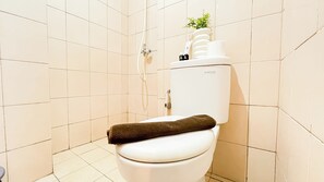 Inodoro blanco con una toalla en el asiento, tanque de agua y una planta encima.