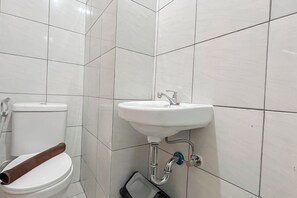 Ein Badezimmer mit Toilette, Waschbecken und Dusche – alles in Weiß.