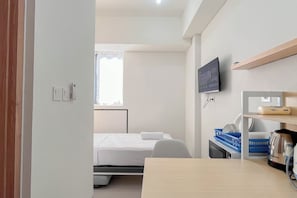 Ein Hotelzimmer mit einem Bett, einem an der Wand befestigten Fernseher, einem Schreibtisch mit Wasserkocher und einem Fenster mit Vorhängen.