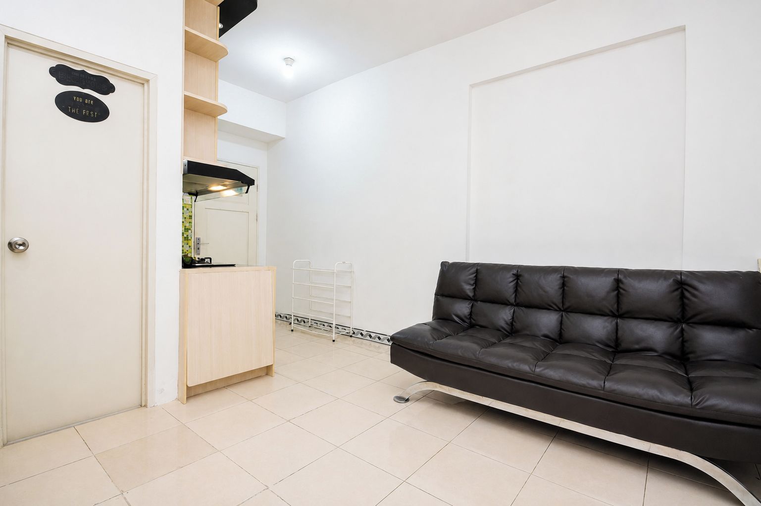 A room with a black leather sofa, a wooden cabinet, a white door, and a white wall.