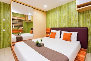 A hotel room with a large bed, a bedside table with a vase and flowers, and a mirror reflecting the room. - 1Br Apartment For 2 Pax At Teluk Intan (Jakarta)