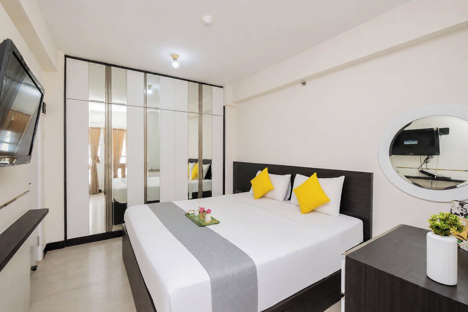 A hotel room with a bed, bedside table, TV, wardrobe, and a mirror.