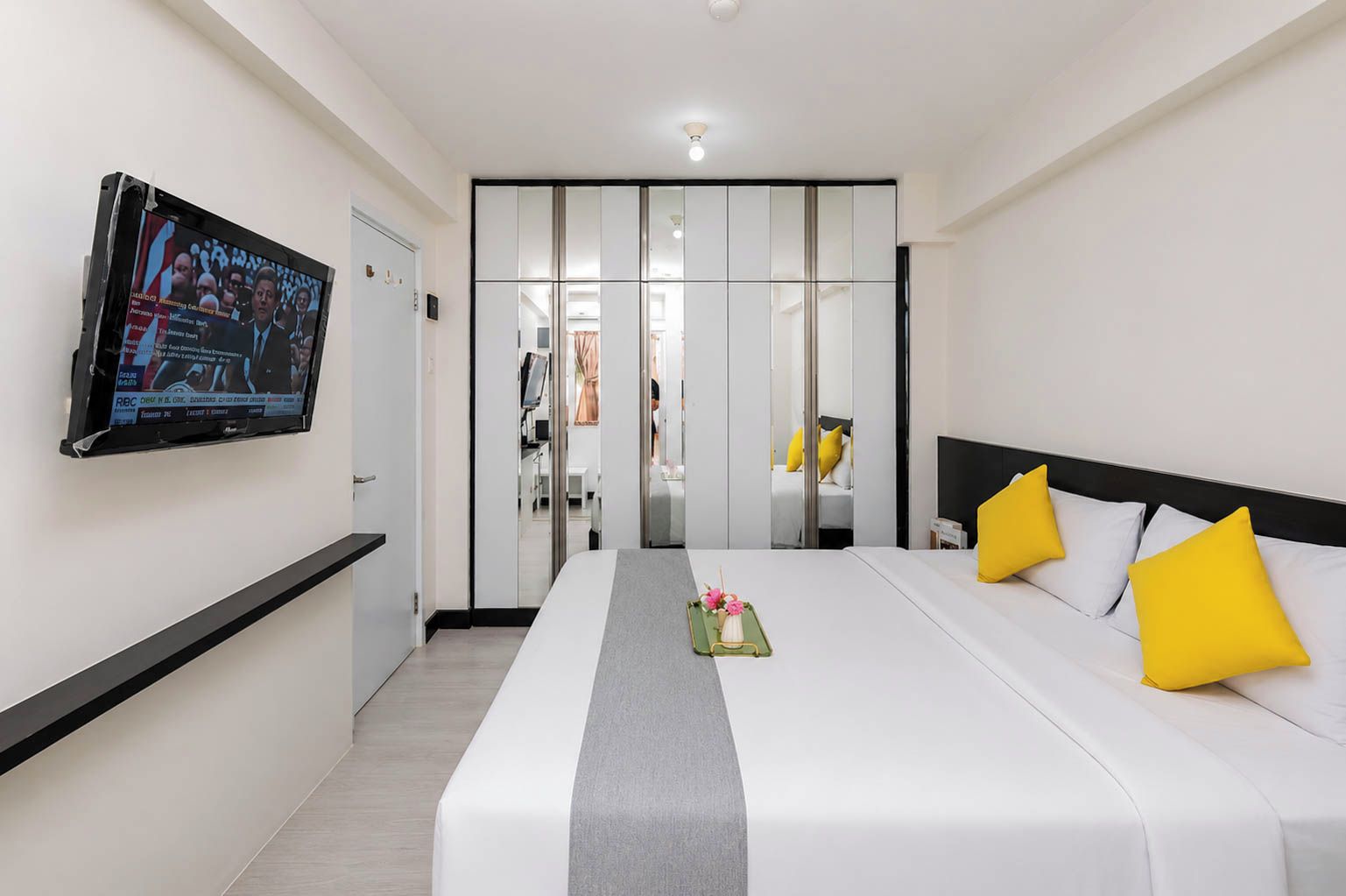 A hotel room with a bed, a television, a mirror, and a sliding door leading to a bathroom.