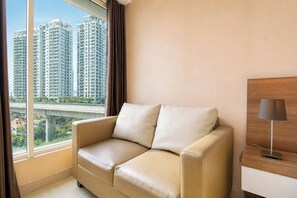 Ein Hotelzimmer mit einem beigefarbenen Sofa, einer Lampe und Blick auf hohe Gebäude.