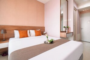 Une chambre d’hôtel avec un grand lit, une table de chevet avec une lampe, un miroir et une petite étagère ornée d’objets décoratifs.