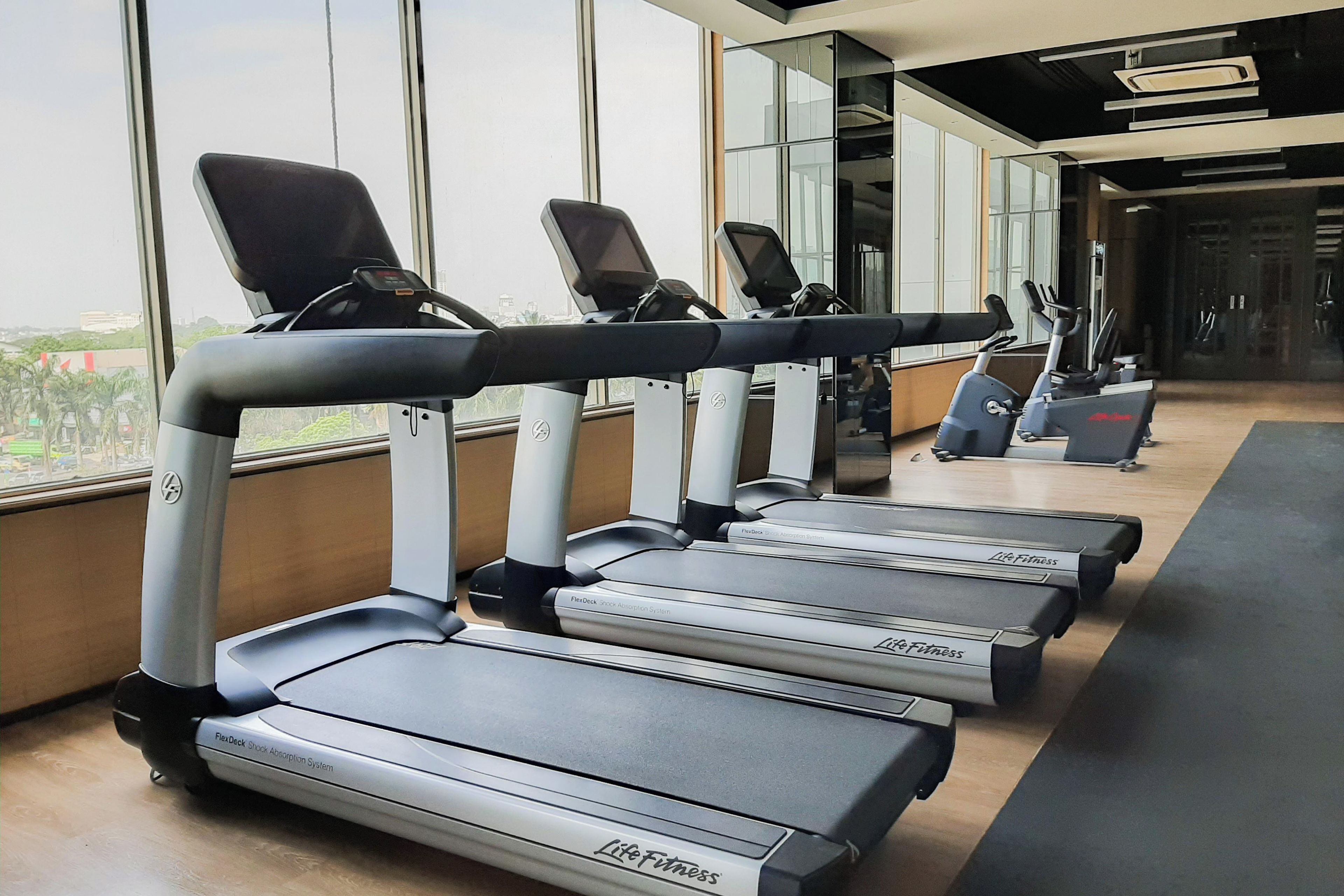 Varias cintas de correr en un gimnasio con amplias ventanas.