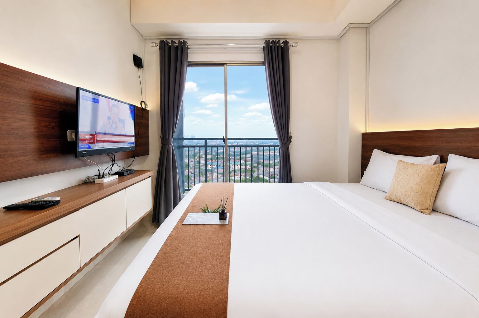 Habitación de hotel con cama, televisor sobre una consola de madera, balcón con vistas y ventana con cortinas.