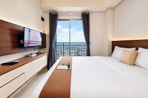 Ein Hotelzimmer mit Bett, Fernseher auf einer Holzkonsole, einem Balkon mit Blick und einem Fenster mit Vorhängen.