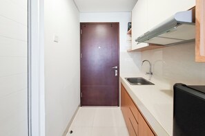A narrow kitchen with a brown door, a sink, and a microwave. - Smart Living Studio At Apartment Springwood Residence Tangerang (Tangerang)