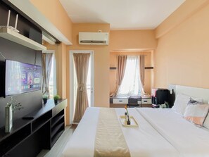 Ett hotellrum med en säng, en tv som är monterad på väggen, ett skrivbord med en stol och en luftkonditioneringsanläggning.