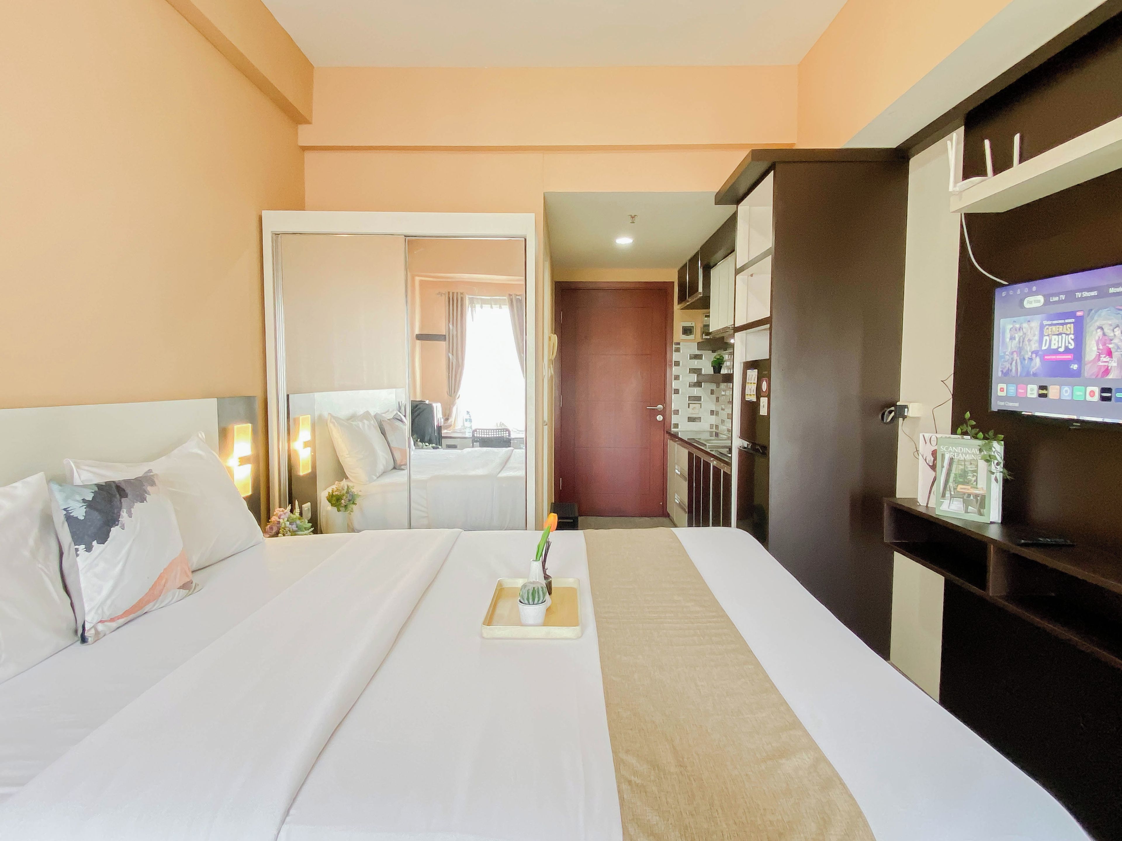 A hotel room with a bed, bedside table, TV, and a mirror.
