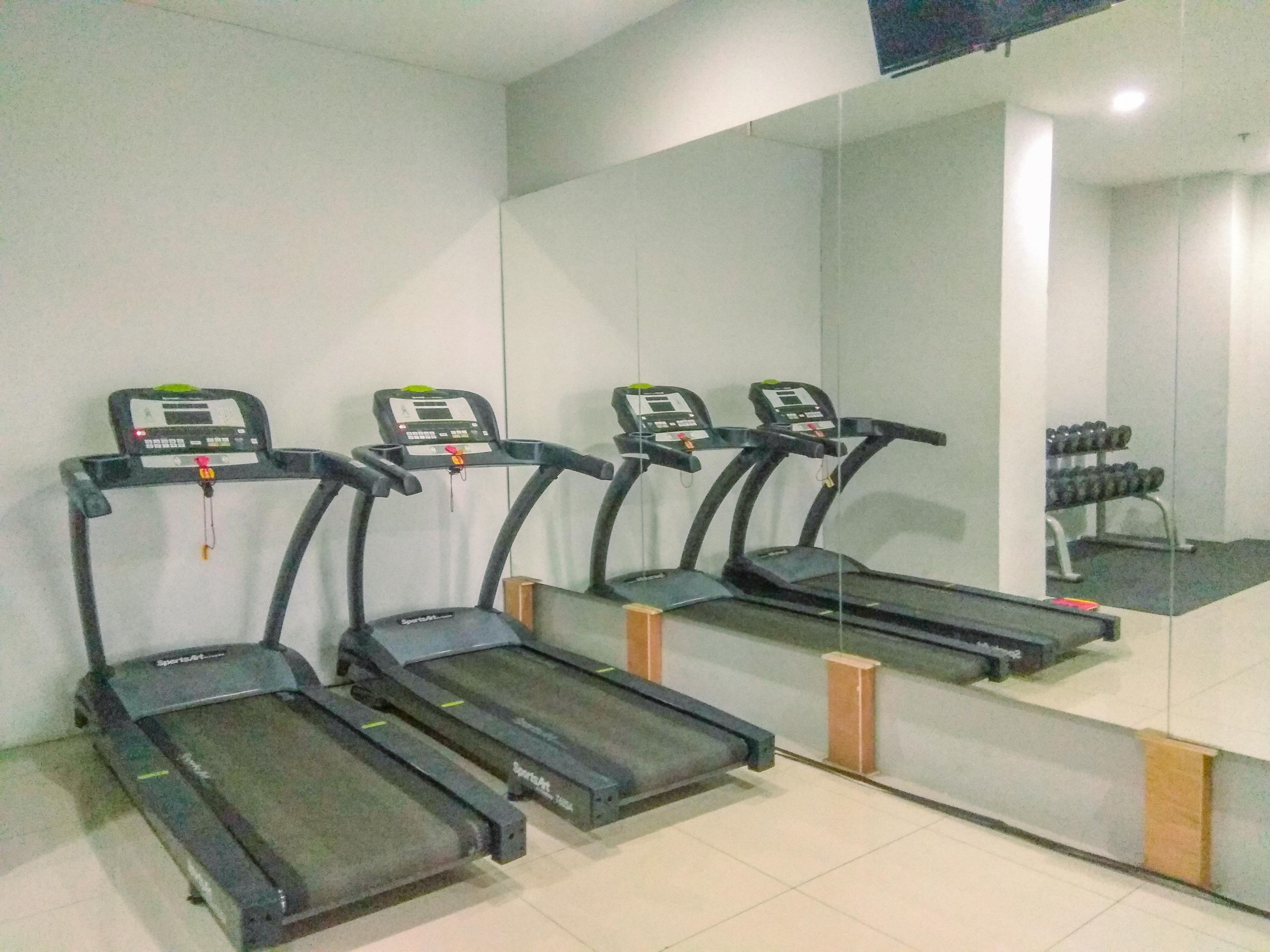 Three treadmills aligned against a wall with a large mirror reflecting the room.