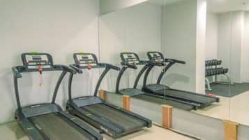 Three treadmills aligned against a wall with a large mirror reflecting the room.