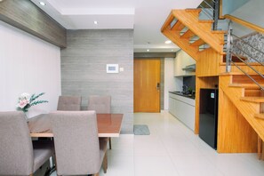 A modern kitchen with a wooden staircase, a dining area with a table and chairs, and a small white appliance on the wall. - Elegant 2Br Loft Apartment Maqna Residence (Jakarta)