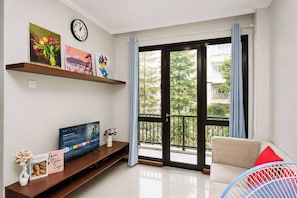 A modern living room with a flat-screen TV, a sofa, a coffee table, and a balcony with a view of the neighborhood. - Homey And Roomy 3Br At Apartment Asatti (Tangerang)