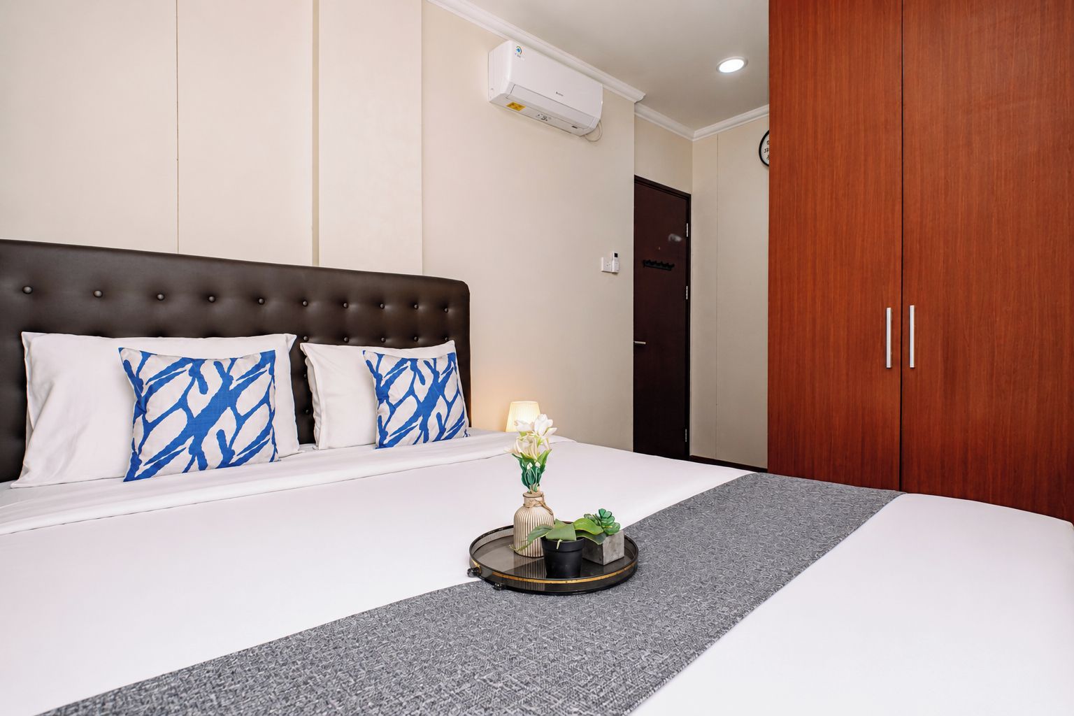 Ein Hotelzimmer mit Bett, Nachttisch mit Vase und Pflanze, Kleiderschrank und Klimaanlage.