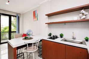 A modern kitchen with a central island, a dining area with a chair, and a view through a large window. - Homey And Roomy 3Br At Apartment Asatti (Tangerang)