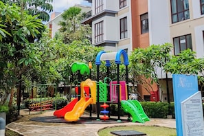 A playground with slides and climbing structures, surrounded by greenery and residential buildings. - Homey And Roomy 3Br At Apartment Asatti (Tangerang)