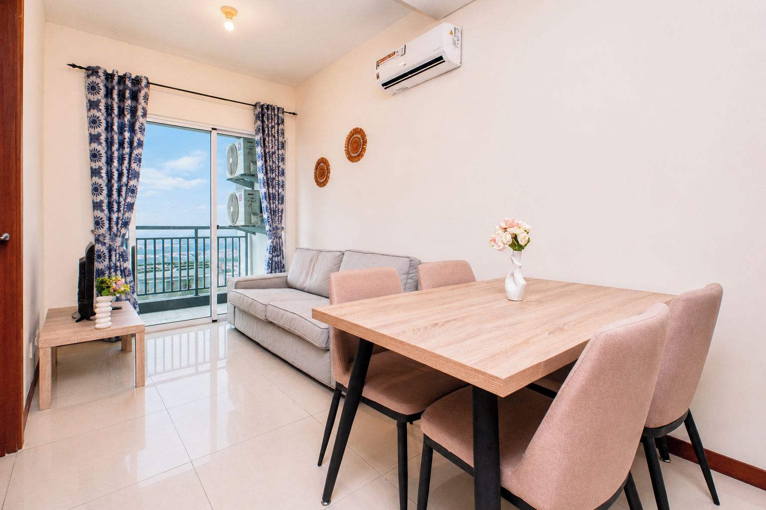 Uma sala de estar moderna com sofá, mesa de jantar com cadeiras, TV e varanda com cortinas.