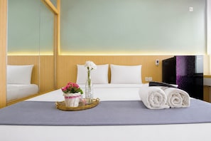 A hotel room with a bed, a television, a tray with a vase of flowers, and rolled towels. - Compact And Stylish Studio At Apartment Pavilion Permata (Surabaya)