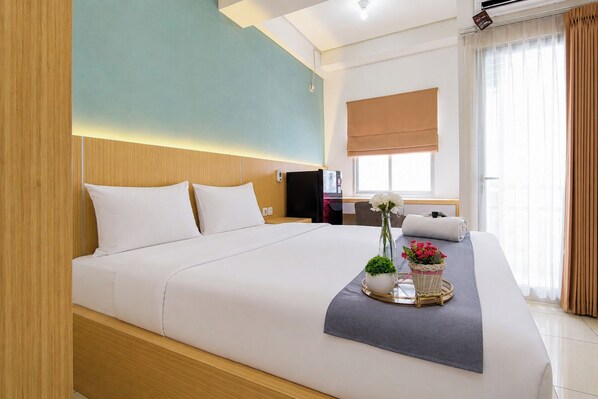 A hotel room with a large bed, a bedside table, a desk, and a window with curtains. - Compact And Stylish Studio At Apartment Pavilion Permata (Surabaya)