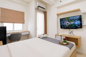 A hotel room with a bed, desk, chair, TV, air conditioning unit, and a window with curtains. - Compact And Stylish Studio At Apartment Pavilion Permata (Surabaya)