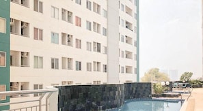 A multi-story residential building with balconies, a swimming pool, and a stone wall. - Compact And Stylish Studio At Apartment Pavilion Permata (Surabaya)