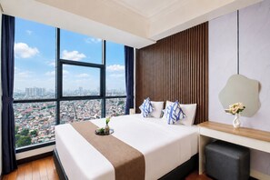 A hotel room with a large bed, a wooden panel wall, a view of the city, and a small table with a vase. - Fully Furnished And Homey 2Br Apartment At Casa Grande Residence (Jakarta)