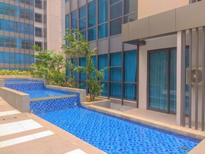A modern building with a swimming pool, surrounded by greenery and featuring large windows. - Fully Furnished And Homey 2Br Apartment At Casa Grande Residence (Jakarta)