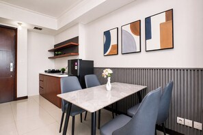 A modern kitchen with a dining area, featuring a marble table, grey chairs, and abstract wall art. - Fully Furnished And Homey 2Br Apartment At Casa Grande Residence (Jakarta)