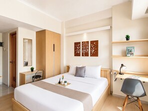 A modern hotel room with a bed, bedside table, desk, chair, and a wall with decorative panels. - Comfortable Studio Apartment At Margonda Residence 2 (Depok)