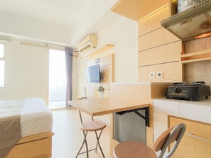 A compact hotel room with a bed, a small kitchenette, a desk with a chair, and a TV mounted on the wall. - Comfortable Studio Apartment At Margonda Residence 2 (Depok)