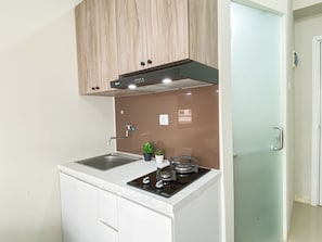A compact kitchen with a white countertop, a stainless steel sink, a gas stove, and wooden cabinets. - Good Homey 2Br At Apartment Green Pramuka City (Jakarta)